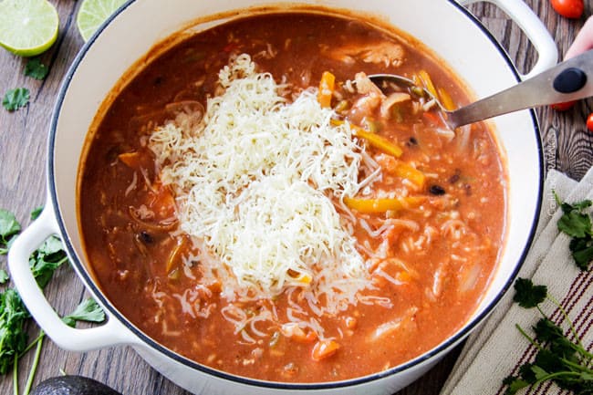 process shot showing how to make chicken fajita soup by adding shredded cheese into Mexican chicken and rice soup.
