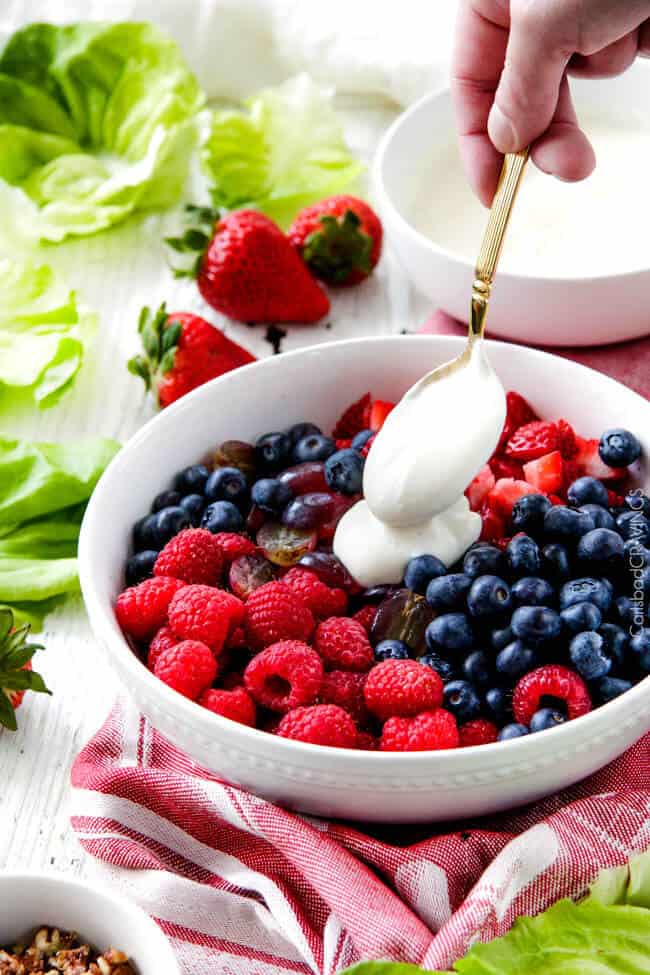 Adding Honey Mascarpone to Berry fruit Salad in white bowl.