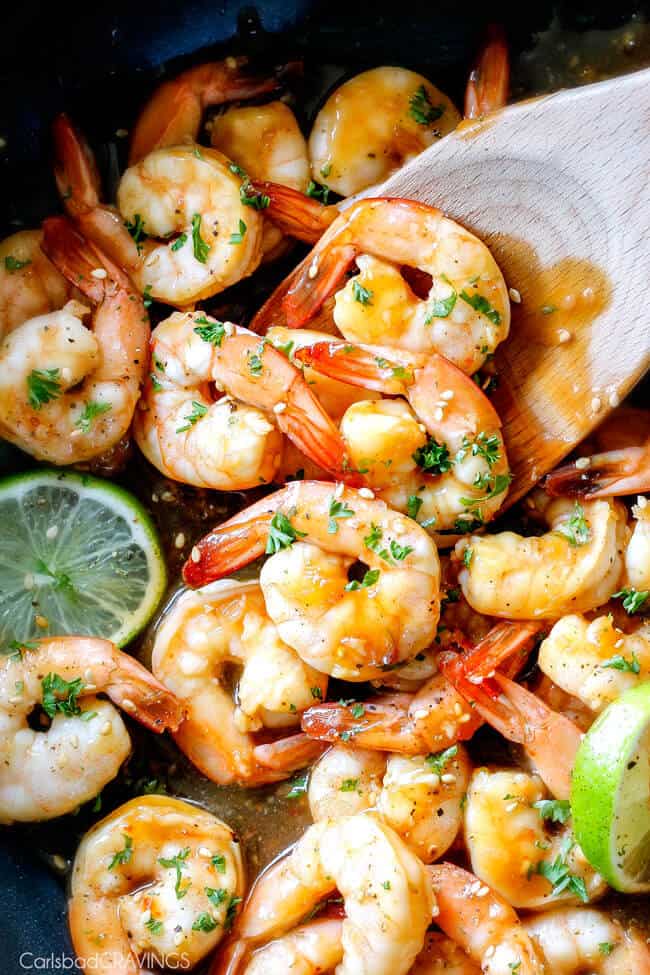 Close up of Sweet Chili Shrimp with lime garnish in a pan with a wooden spoon.