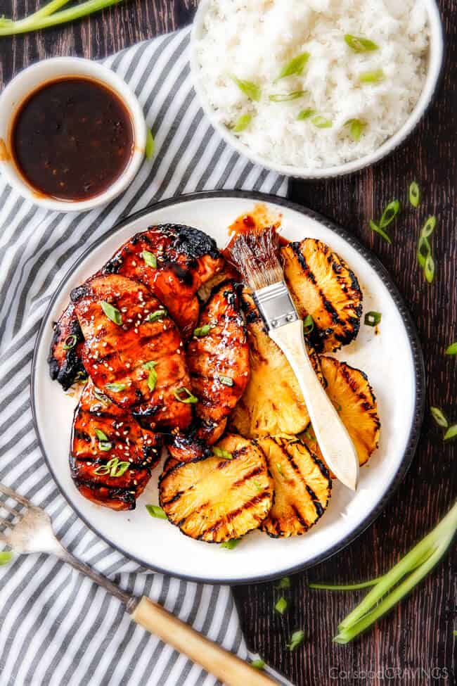 5 Minute prep Easy Teriyaki Chicken infused with Sweet Chili Sauce for added depth of flavor and YUM! The marinade doubles as the sauce for an easy family favorite that tastes better than takeout! My family loves this with rice and stir fried veggies and I love it on salad or in wraps! top view of grilled teriyaki chicken breasts on a white plate