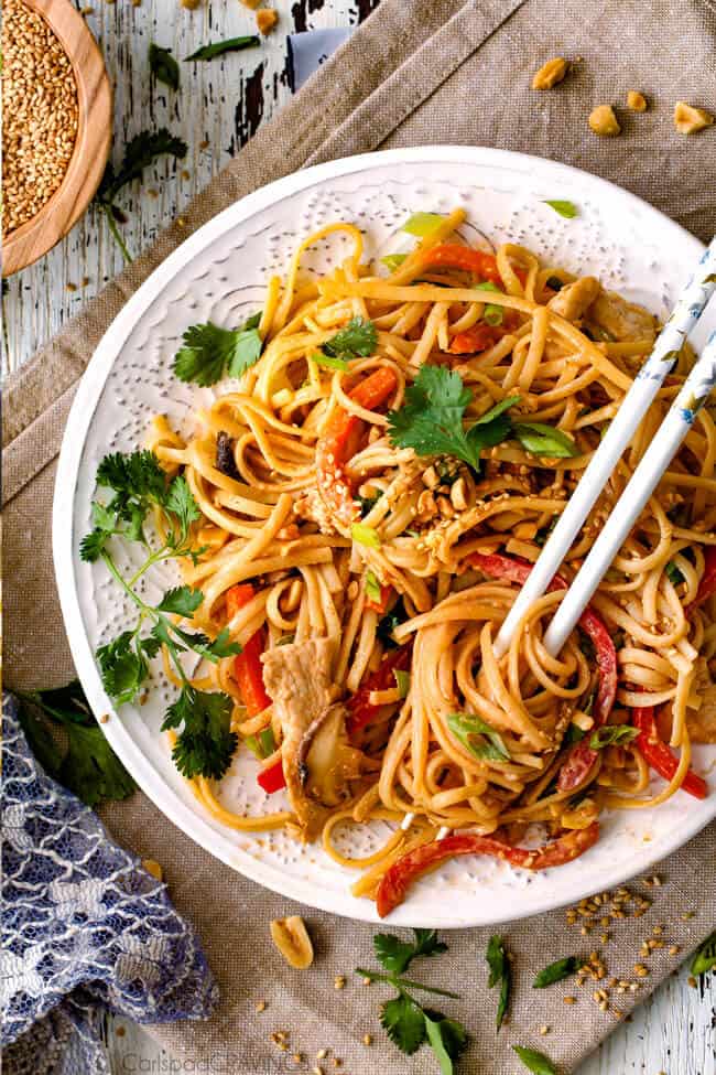 30 Minute Peanut Sesame Noodles (with Chicken and Veggies) - super quick and easy meal all in one with the most amazing creamy peanut sesame sauce you will crave for days! Top view of sesame noodles with chicken on a white pate with chicken, cilantro and peanuts