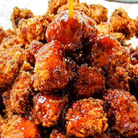 showing how to make Chinese Lemon Chicken by drizzling fried chicken pieces with lemon sauce