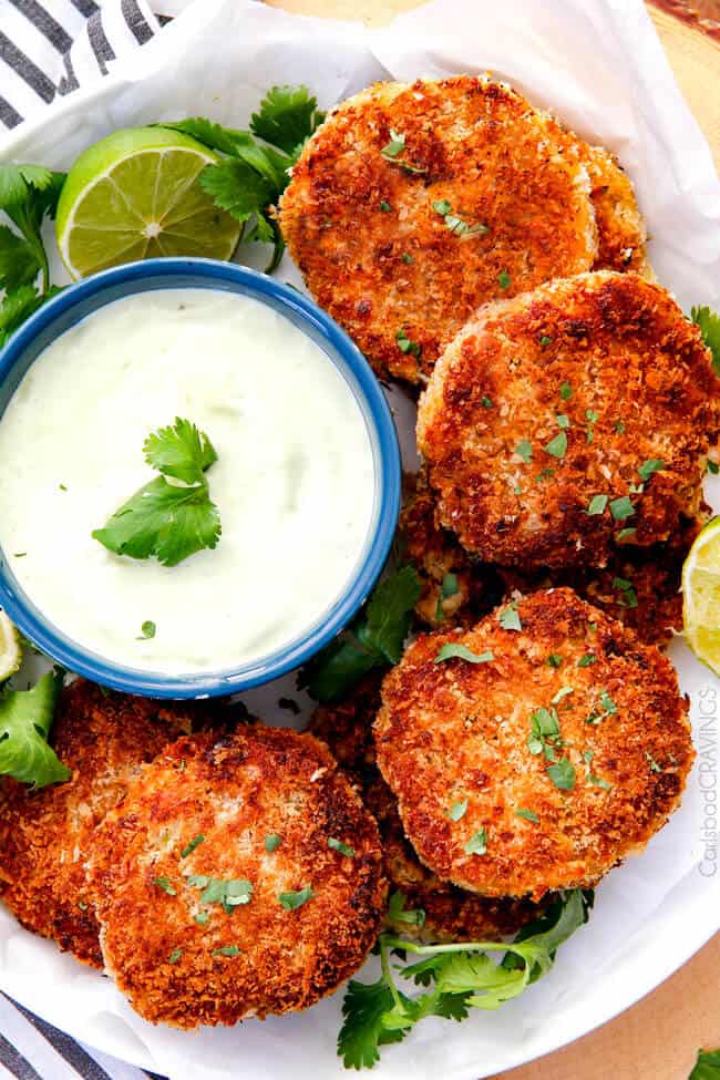 Easy, extra crispy, restaurant quality Crab Cakes right in your own home! Crispy on the outside, moist, juicy, flavor packed on the inside with the BEST DIP ever!! You can also make ahead of time for stress free appetizers! top view of best crab cake recipe with crab cake sauce in a white serving dish with lemon garnish