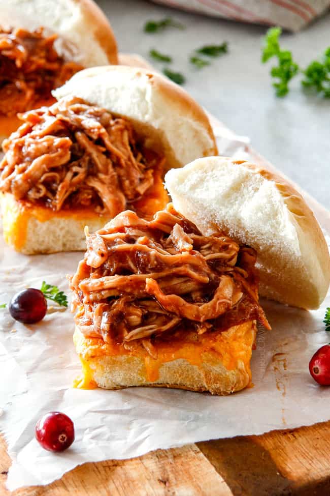 20 Minute Chipotle BBQ Cranberry Turkey Sliders (or chicken!) are a wonderfully delicious way to devour your Thanksgiving turkey leftovers or SO good you will want to make them forever and ever with chicken! And don’t skip the crunchy, sweet and tangy out of this world Apple Poppy Seed Slaw! a row of pulled turkey sliders on a cutting board