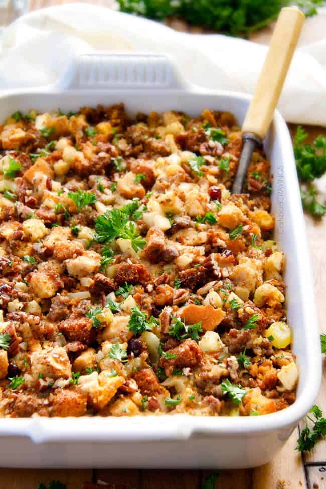 Thanksgiving Cornbread Sausage Stuffing (Dressing) with dried cranberries, apples and pecans is is destined to become your new go-to recipe!! The wonderfully savory, buttery herb infused stuffing is moist, flavorful, easy and absolutely addicting! a white casserole dish of Thanksgiving Cornbread Sausage Stuffing garnished with parsley