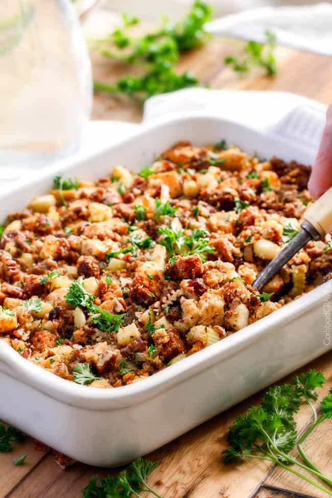 Thanksgiving Cornbread Sausage Stuffing (Dressing) with dried cranberries, apples and pecans is is destined to become your new go-to recipe!! The wonderfully savory, buttery herb infused stuffing is moist, flavorful, easy and absolutely addicting! far away shot of a spoon scooping up easy cornbread stuffing