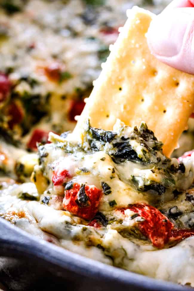 Brie Spinach Dip - my friends could not get over this appetizer! Its your favorite spinach dip made even more delicious with BRIE! Creamy, cheesy and so addicting! up close of dipping a cracker in baked spinach dip with cheese