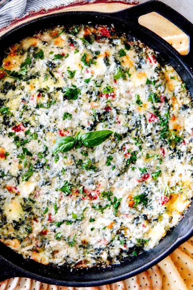 Brie Spinach Dip - my friends could not get over this appetizer! Its your favorite spinach dip made even more delicious with BRIE! Creamy, cheesy and so addicting! Top view of cheesy baked spinach dip with cream cheese or brie in a cast iron skillet with crackers and bread around it