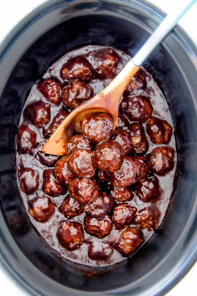 Tender juicy, sweet and spicy Slow cooker Korean Meatballs simmered in the most tantalizing sweet heat sauce that everyone goes crazy for! Perfect appetizer or delicious, easy meal with rice! top view of crockcpot Korean Meatballs covered in Korean BBQ Sauce in the slow cooker with a wood serving spoon holding some of the meatballs