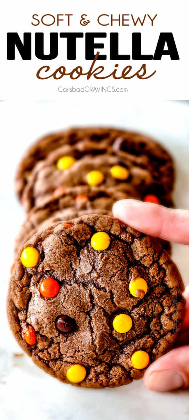 These Super soft and chewy Nutella Cookies are my absolute favorite chocolate cookie with a whole cup of Nutella mixed right into the batter! Mix in anything you want from chocolate chips to, Reese's pieces to Andes mints for the perfect Christmas cookie! up close of holding chewy Nutella cookies with Reese's pieces