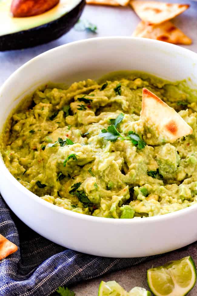 This creamy Avocado Hummus is SO addicting and only 3 ingredients! Its crazy flavorful, healthy and super easy! side view of a big white bowl of healthy avocado hummus surrounded by pita chips