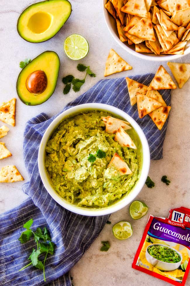 This creamy Avocado Hummus is SO addicting and only 3 ingredients! Its crazy flavorful, healthy and super easy! top view of avocado hummus keto with sliced avocados and seasonings next to the white bowl