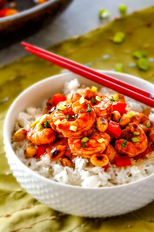 This easy, healthy, Kung Pao Shrimp tastes better than takeout and is on your table in less than 30 minutes! I was licking my plate of the savory spicy sauce! a white bowl full of rice and easy Kung Pao Shrimp with peanuts and green onions and red chopsticks