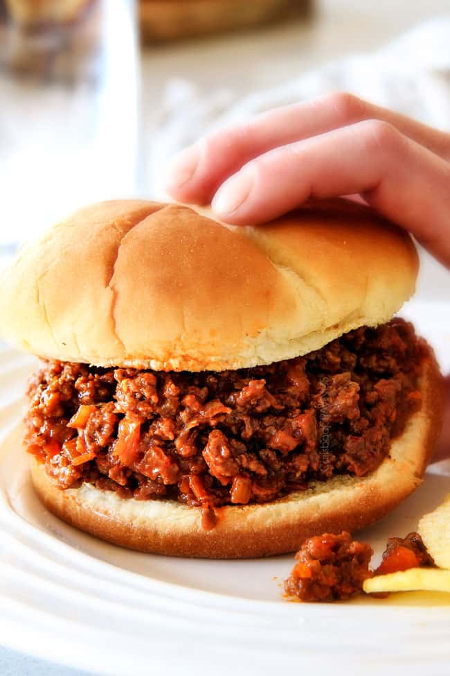 a hand picking up a Sloppy Joe with filling spilling out