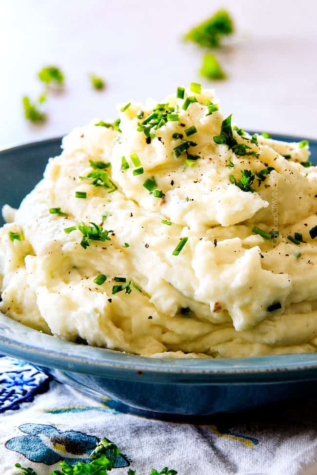 BEST EVER Creamy Company Mashed potatoes infused with butter, garlic, and Parmesan! I could eat these all day alone with a spoon - they are incredibly velvety, flavorful and so good everyone will beg you for the recipe! front view of a tall bowl of garlic mashed potatoes with butter, garlic, sour cream, Parmesan, chives, salt, pepper and heavy cream