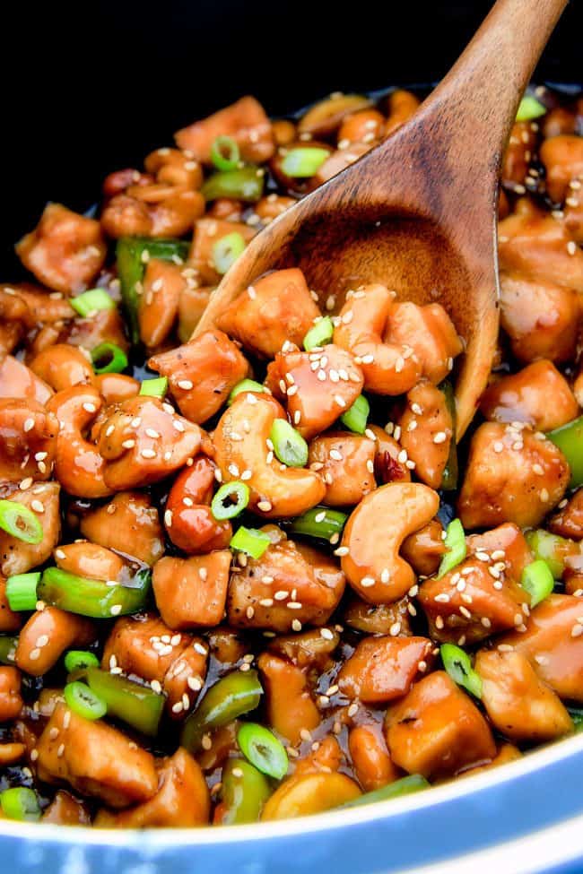 Slow Cooker Chinese Cashew Chicken- this is the best cashew chicken I have ever tried! the chicken is incredibly tender, the sauce is wonderfully flavorful and the punch of buttery, creamy cashews is out of this world! Definitely a family favorite and so much heather than takeout! up close of a wooden spoon serving Slow Cooker Chinese Cashew Chicken recipe with vegetables