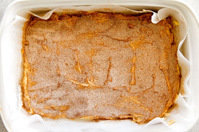 Incredibly EASY, thick, soft and chewy, buttery Snickerdoodle Cookie Bars taste just like the cookie but so much easier and less time consuming! The cinnamon and sugar crackle top is to die for! Showing how to make Sninckerdoodle Bars by sprinkling bottom of pan with cinnamon and sugar and topping with half of the dough.