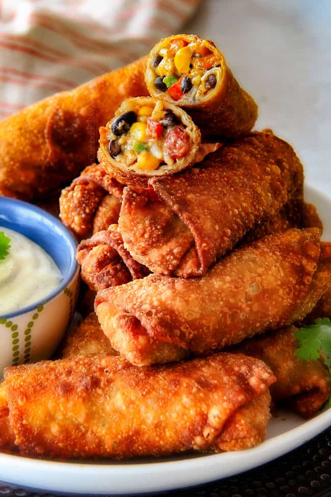 CRISPY Southwest Egg Rolls loaded with Mexican spiced chicken, beans, tomatoes, rice, avocado and cheese! These egg rolls are unreal! So much flavor and texture! And don't skip the Cilantro Lime Ranch Dip - its heaven! a stack of fried Southwest Egg Rolls on a plate with Cilantro Dip