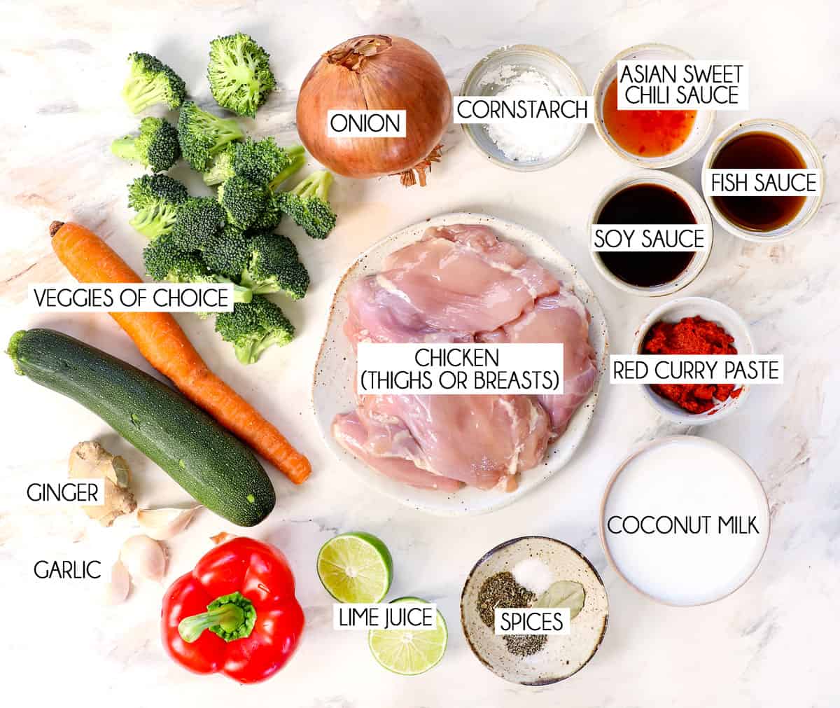 top view of chicken curry ingredients: chicken thighs, red curry paste, fish sauce, soy sauce, lime juice, coconut milk, onions, broccoli, carrots, ginger, garlic and bell peppers