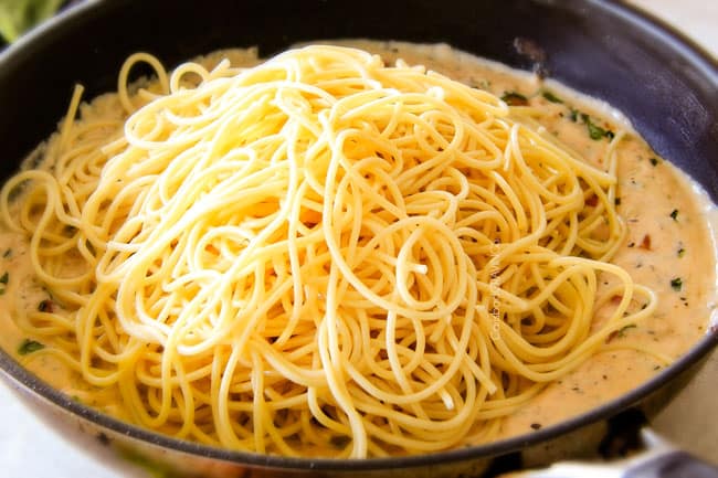Adding pasta to the sauce showing how to make Garlic Mozzarella Margherita Pasta with basil.