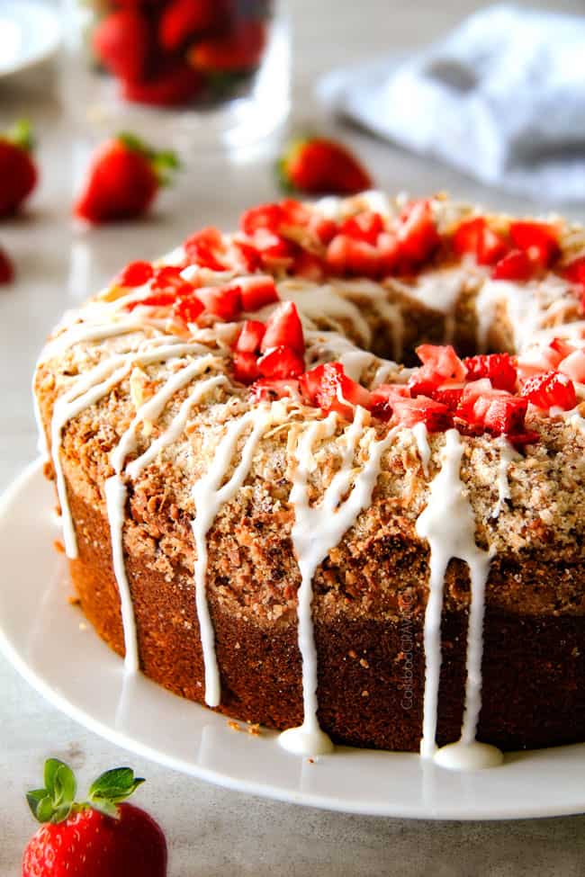 Strawberry Cream Cheese STUFFED Sour Cream Coffee Cake - this is the best strawberry coffee cake ever! the INCREDIBLY creamy cheesecake-like cream cheese filling and strawberries all topped with Coconut Pecan Streusel and Lemon Drizzle is OUT OF THIS WORLD! I can't say enough good things about this coffee cake! side view of cream cheese Coffee Cake with streusel and glaze on a white plate