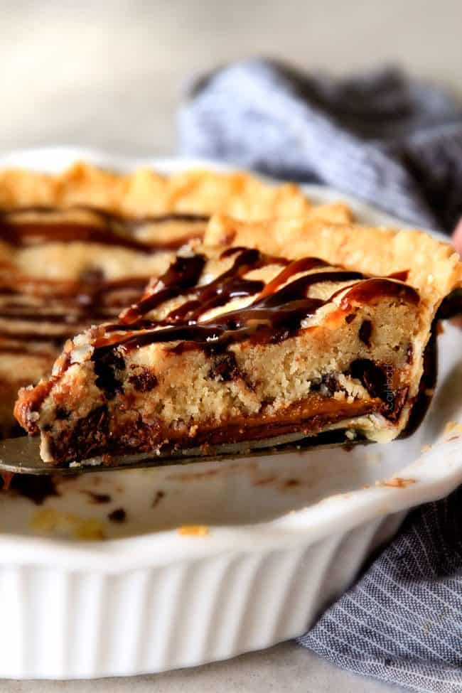make ahead Million Dollar Cookie Pie layered with Nutella, Dulce de Leche and cookie dough! This is hands down the best skillet cookie I've ever made and its always such a crowd pleaser! taking out a slice of gooey chocolate chip cookie pie with a pie server