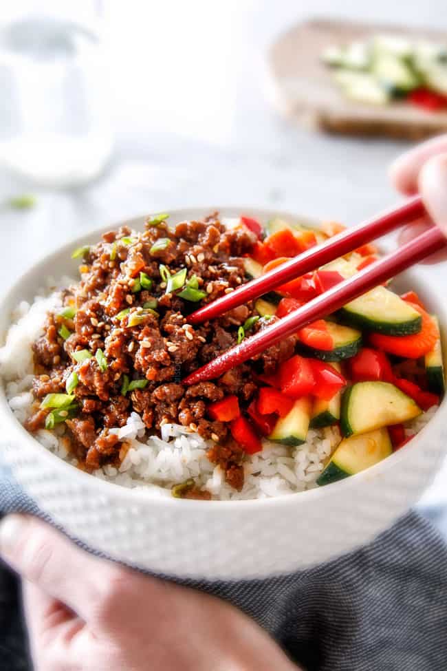 30 Minute Korean Beef Bowls are my absolute favorite last minute dinner! bursting with flavor and one of the absolute easiest meals you will ever make! chopsticks taking a bite of ground beef from a Korean Beef Bowl with Veggies