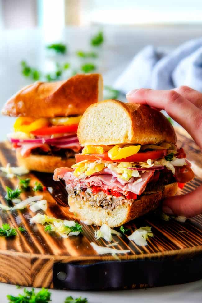 Easy, customizable LOADED Slow Cooker Italian Beef Sandwiches are crazy tender, seeping with flavor and unbelievably delicious! They make the easiest dinner or party food and super fun (make ahead!) sandwich bar! the best Italian Beef Sandwich sliced in half with a hand holding the sandwich