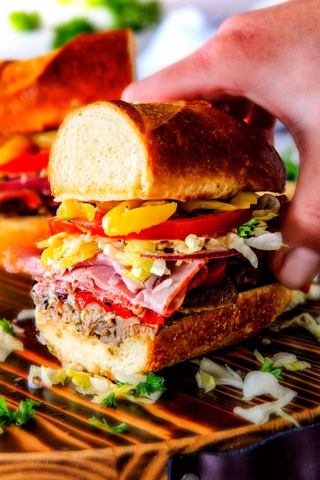 Easy, customizable LOADED Slow Cooker Italian Beef Sandwiches are crazy tender, seeping with flavor and unbelievably delicious! They make the easiest dinner or party food and super fun (make ahead!) sandwich bar! up close of a hand holding half of an easy Italian Sandwich