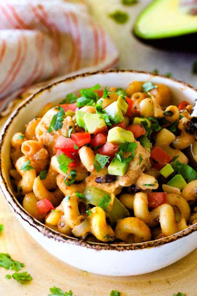 Lighter ONE POT Chicken Fajita Pasta has only minutes of hands-on cooking time! Its smothered in cheesy, creamy salsa infused sauce bursting with your favorite fajita spiced chicken, onions and peppers! The pasta cooks right IN the sauce for simple prep, minimal cleanup, and extra flavooooor! a bowl of cheesy chicken fajita pasta garnished with avocados and tomatoes.