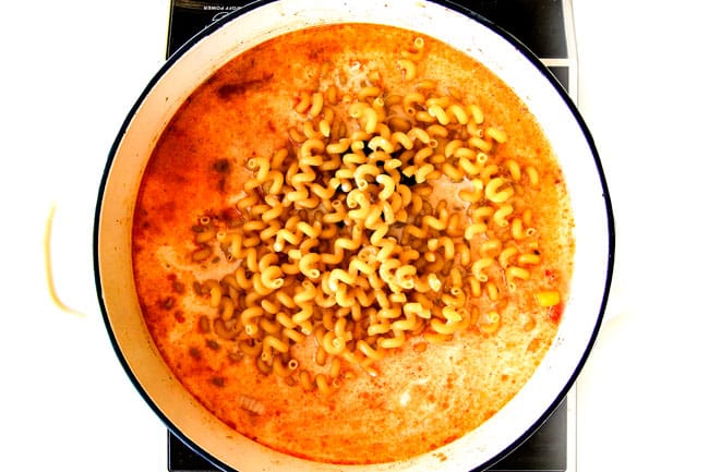 Lighter ONE POT Chicken Fajita Pasta has only minutes of hands-on cooking time! Its smothered in cheesy, creamy salsa infused sauce bursting with your favorite fajita spiced chicken, onions and peppers! The pasta cooks right IN the sauce for simple prep, minimal cleanup, and extra flavooooor! showing how to make healthy Chicken Fajita Pasta by adding pasta to pot with milk, salsa and enchilada sauce.