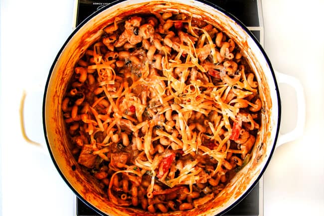 Lighter ONE POT Chicken Fajita Pasta has only minutes of hands-on cooking time! Its smothered in cheesy, creamy salsa infused sauce bursting with your favorite fajita spiced chicken, onions and peppers! The pasta cooks right IN the sauce for simple prep, minimal cleanup, and extra flavooooor! showing how to make chicken fajita pasta by adding cheese and sour cream to the pot.