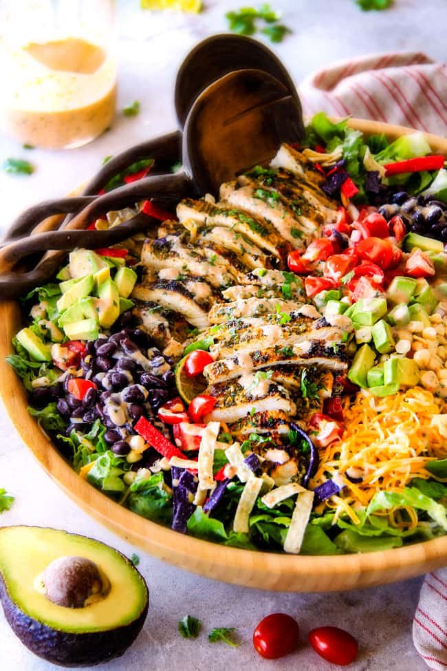 I couldn't stop eating this Cilantro Lime Chicken Taco Salad! Its bursting with tender, juicy chicken and the sweet & tangy Creamy Baja Catalina Dressing is out of this world delicious! This combo is pure heaven! side view of best chicken taco salad in a wood bowl with black beans, corn, tomatoes, avocados, cheese and tortilla strips