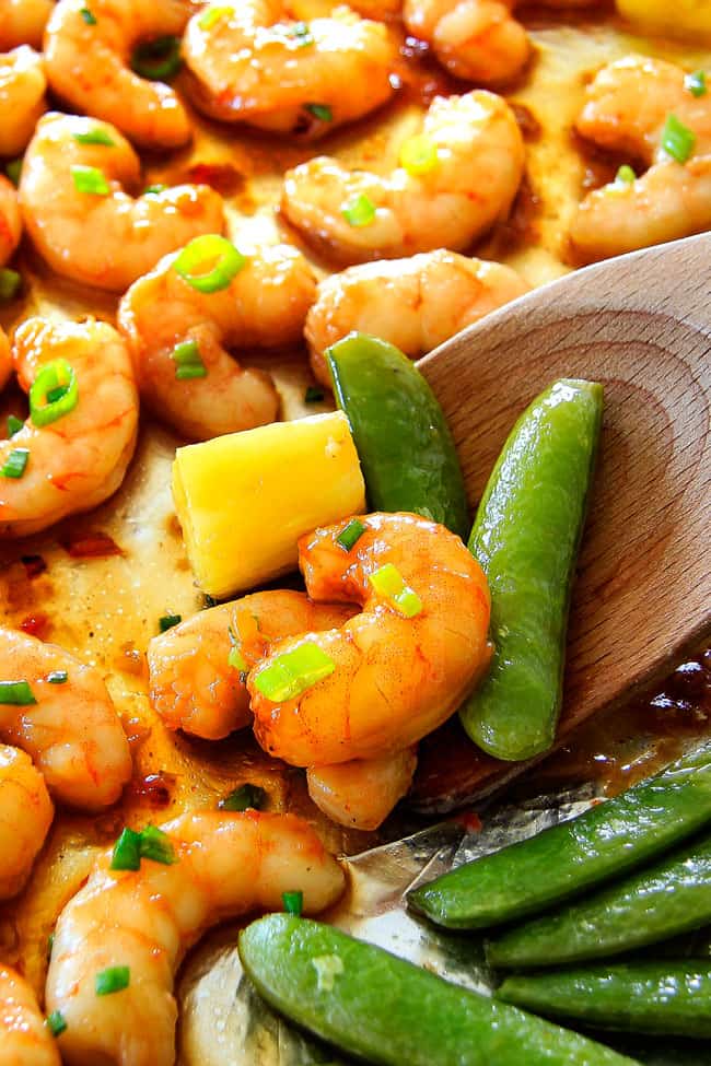 I am in love with this Sheet Pan Teriyaki Shrimp, Pineapple and Snap Peas! Its SO easy, healthy, a meal-in-one and the homemade Teriyaki sauce is the best I've ever had (DON'T be tempted to use store bought!)! I'm always keeping frozen shrimp on hand so I can make this any time! a wooden spoon picking up some teriyaki shrimp