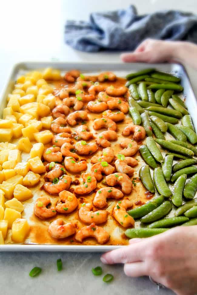 I am in love with this Sheet Pan Teriyaki Shrimp, Pineapple and Snap Peas! Its SO easy, healthy, a meal-in-one and the homemade Teriyaki sauce is the best I've ever had (DON'T be tempted to use store bought!)! I'm always keeping frozen shrimp on hand so I can make this any time! two hands holding a serving tray of easy teriyaki shrimp