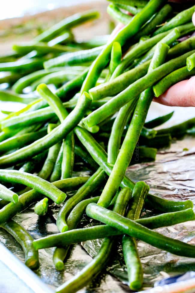 Forget green bean casserole, these wonderfully flavorful, crisp tender Roasted Green Beans with Creamy Gruyere Sauce are AMAZING!!! They the best green beans you will ever eat! They are easy enough for every day but delicious enough for special occasions (like Thanksgiving, Christmas!)! #greenbeancasserole #thanksgivingrecipe showing how to make roasted green beans by tossing fresh green beans with olive oil, salt and pepper
