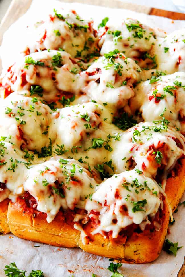 These Cheesy Italian Meatball Sliders are my favorite party food ever and my family loves them for dinner! The meatballs are the BEST (so tender and juicy!) and the marinara is amazing and I love how they are individual sliders instead of meatball subs! I can't recommend these enough! a tray of Italian Meatball Sliders with marinara, mozzarella and fresh parsley