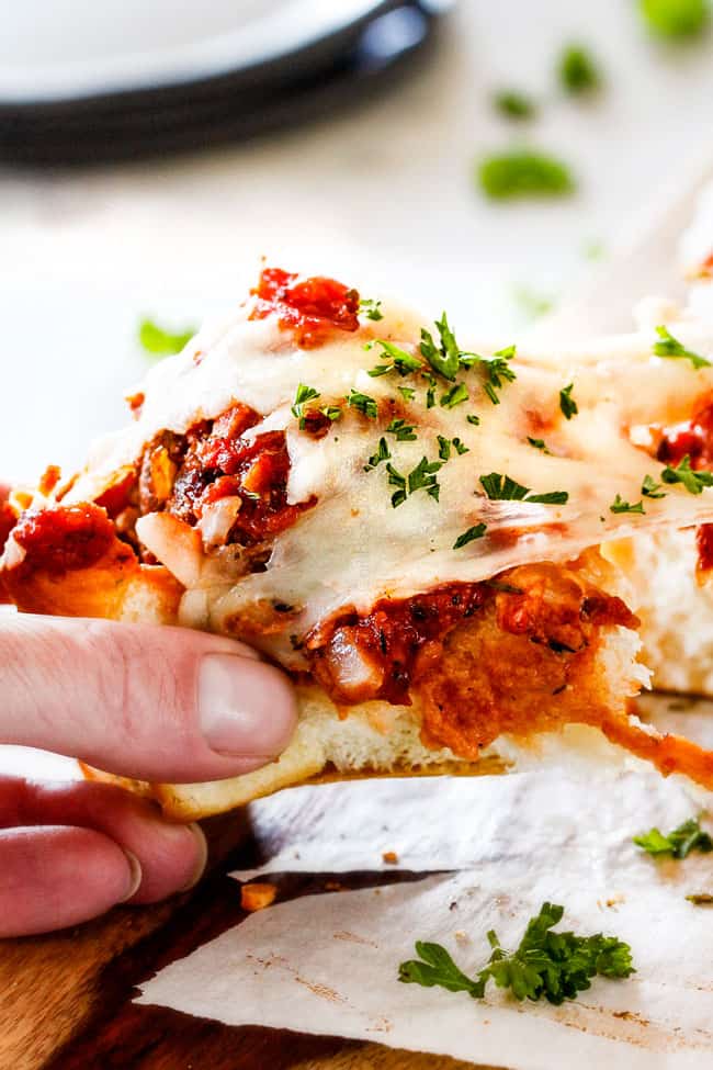 These Cheesy Italian Meatball Sliders are my favorite party food ever and my family loves them for dinner! The meatballs are the BEST (so tender and juicy!) and the marinara is amazing and I love how they are individual sliders instead of meatball subs! I can't recommend these enough! up close view of pulling an Italian meatball sliders on Hawaiian roll away from tray with gooey cheese