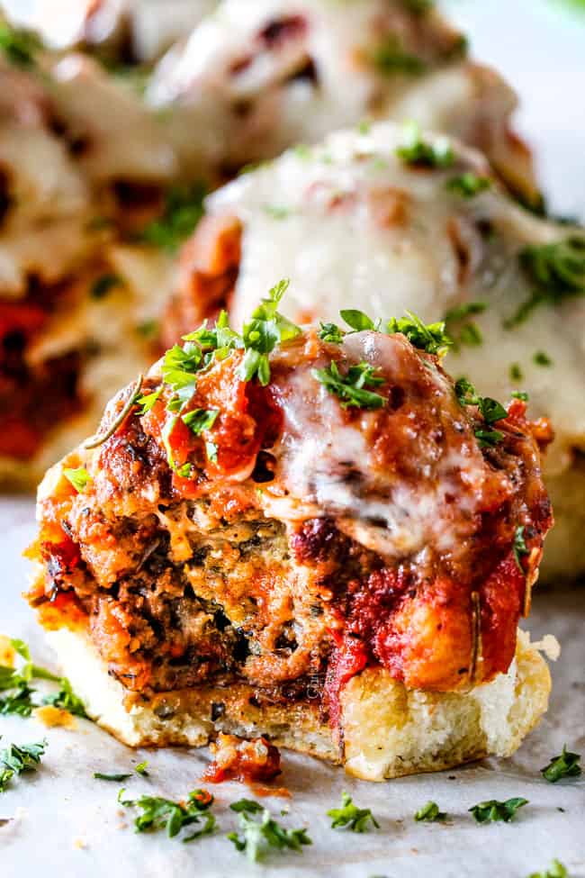These Cheesy Italian Meatball Sliders are my favorite party food ever and my family loves them for dinner! The meatballs are the BEST (so tender and juicy!) and the marinara is amazing and I love how they are individual sliders instead of meatball subs! I can't recommend these enough! meatball slider on a Hawaiian roll with a bite taken out of it with cheese and marinara