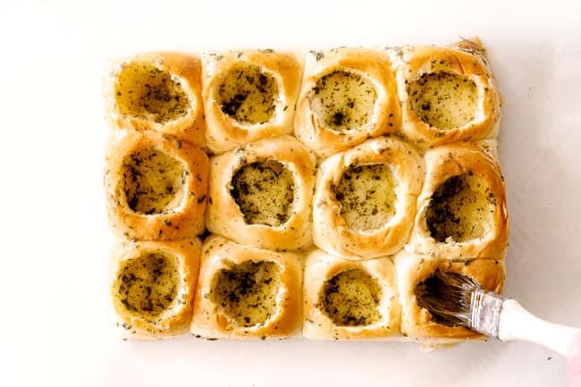 These Cheesy Italian Meatball Sliders are my favorite party food ever and my family loves them for dinner! The meatballs are the BEST (so tender and juicy!) and the marinara is amazing and I love how they are individual sliders instead of meatball subs! I can't recommend these enough! showing how to make meatball sliders by buttering the inside of Hawaiian rolls with butter, parsley and garlic