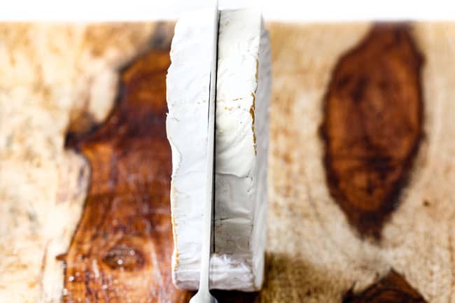 Rich and creamy Baked Brie in Puff Pastry is always a total luxuriously tasting crowd pleaser with minimal effort! (step by step pictures included) It can be prepped in advance then baked when you're ready for company! showing how to make baked brie in puff pastry by slicing brie down the center with a knife