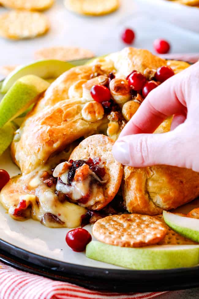 Rich and creamy Baked Brie in Puff Pastry is always a total luxuriously tasting crowd pleaser with minimal effort! (step by step pictures included) It can be prepped in advance then baked when you're ready for company! scooping a bite of baked brie in puff pastry with cranberries with a cracker