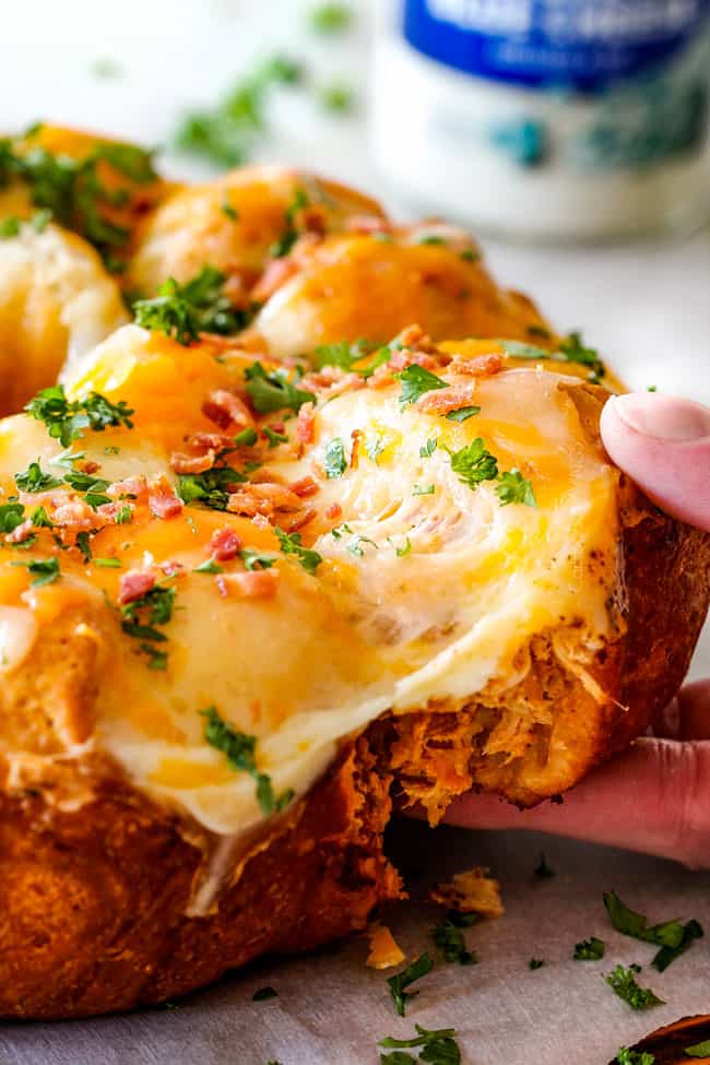 Mega flavorful Buffalo Chicken Pull Apart Bread is your favorite decadent creamy, cheesy dip baked right into a buttery biscuit ring! Crazy delicious EASY crowd pleasing appetizer perfect for parties or game day! It may look super impressive but you won’t believe how easy it is! pulling a cheesy biscuit away from the Buffalo Chicken Pull Apart Bread