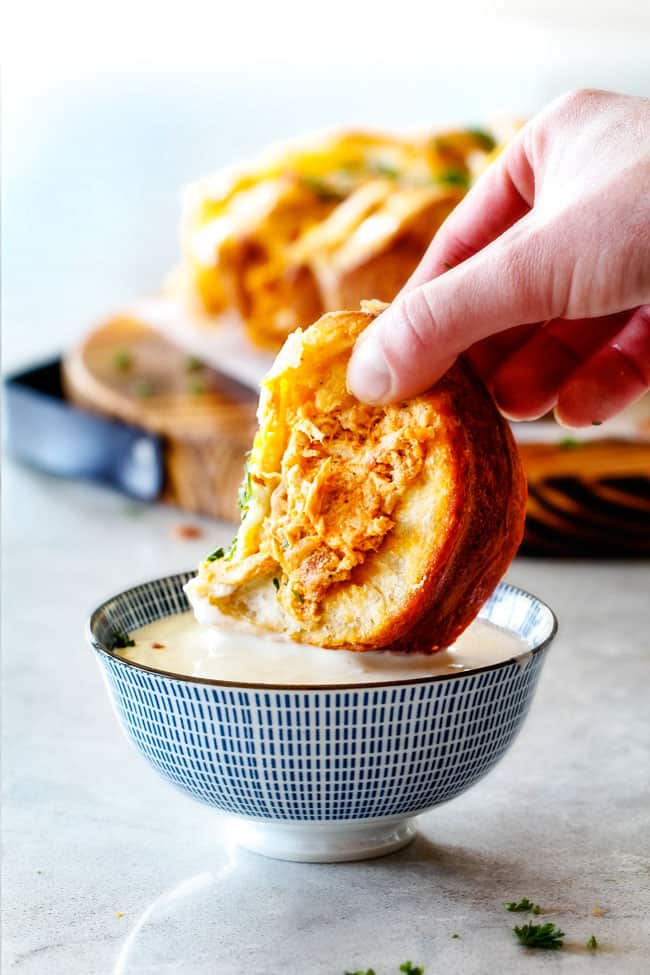 Mega flavorful Buffalo Chicken Pull Apart Bread is your favorite decadent creamy, cheesy dip baked right into a buttery biscuit ring! Crazy delicious EASY crowd pleasing appetizer perfect for parties or game day! It may look super impressive but you won’t believe how easy it is! dipping a piece of Buffalo Chicken Pull Apart Bread in blue cheese dressing