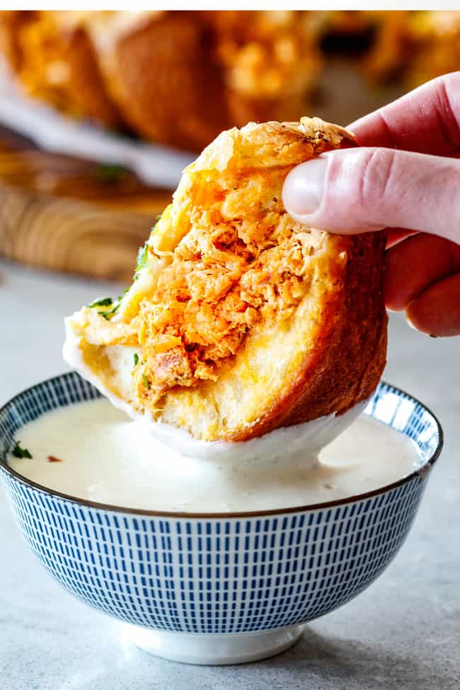Mega flavorful Buffalo Chicken Pull Apart Bread is your favorite decadent creamy, cheesy dip baked right into a buttery biscuit ring! Crazy delicious EASY crowd pleasing appetizer perfect for parties or game day! It may look super impressive but you won’t believe how easy it is! up close of dunking a piece of Buffalo Chicken Pull Apart Bread into blue cheese dressing