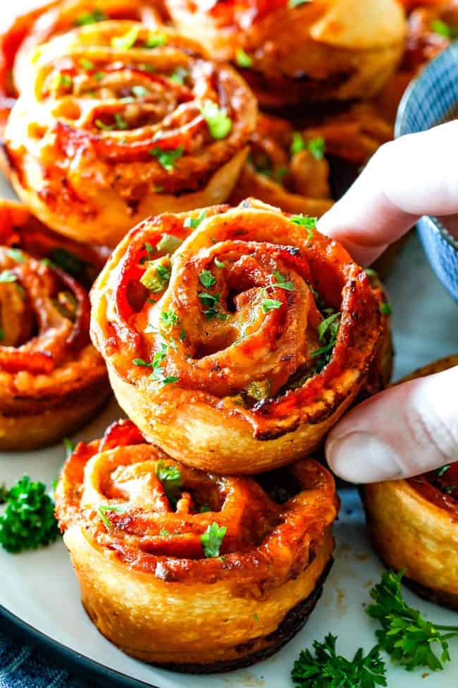 These Pizza Pinwheels are super easy to make, customizable, freeze beautifully, and absolutely irresistible for snacks, appetizers or fun meals! You friends and family will beg you to make these! grabbing a cooked pizza pinwheel from a platter of pizza pinwheels