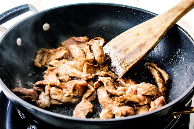 thinly sliced flank steak searing in a black skillet showing how to make beef and broccoli recipe