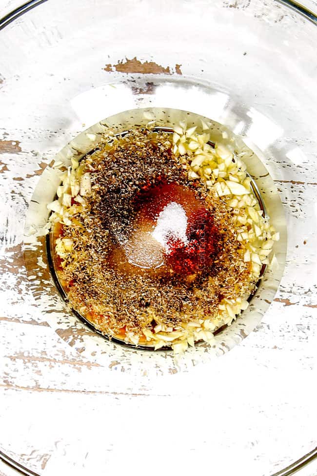 showing how to make Greek Chicken Salad by adding marinade ingredients: lemon juice, balsamic vinegar, garlic and herbs to a glass bowl