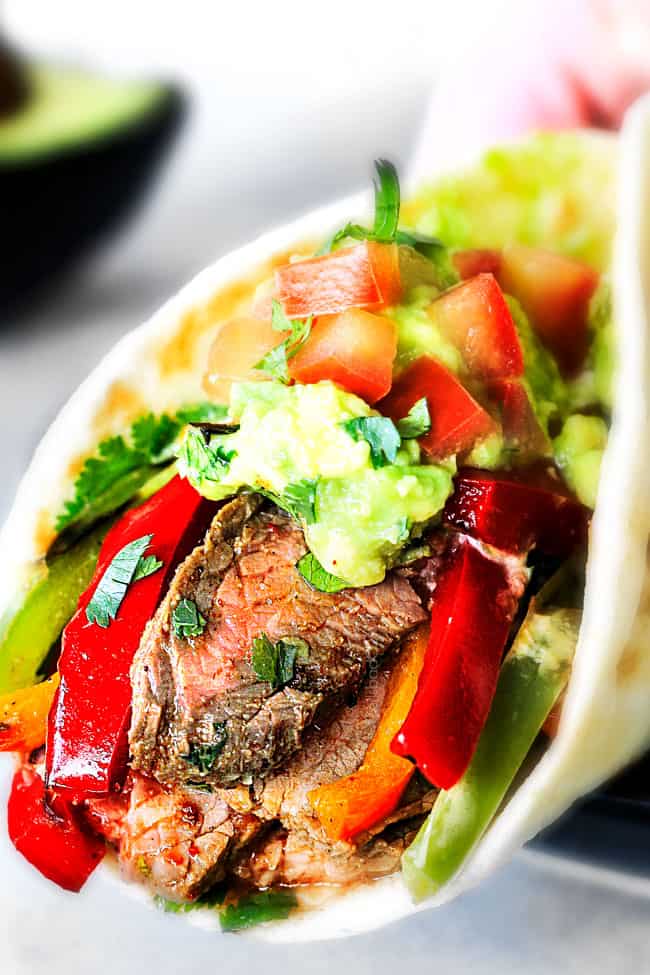 up close showing how to serve steak fajitas by wrapping up with steak, bell peppers, guacamole and pico de gallo