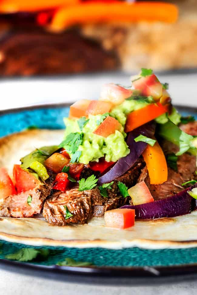 showing how to make steak fajitas by adding grilled steak on top of a flour tortilla with bell peppers, guacamole and pico de gallo